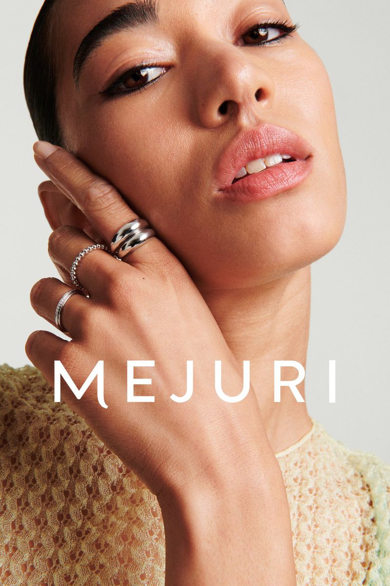 Close-up portrait of a woman wearing silver rings on her hand, photographed for Mejuri against a light background.