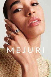 Close-up portrait of a woman wearing silver rings on her hand, photographed for Mejuri against a light background.