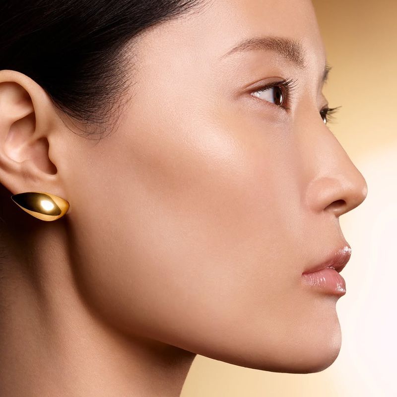 Close-up of a woman with flawless skin wearing gold earrings. Beauty shot with focus on skin texture, eye detail, and warm lighting.