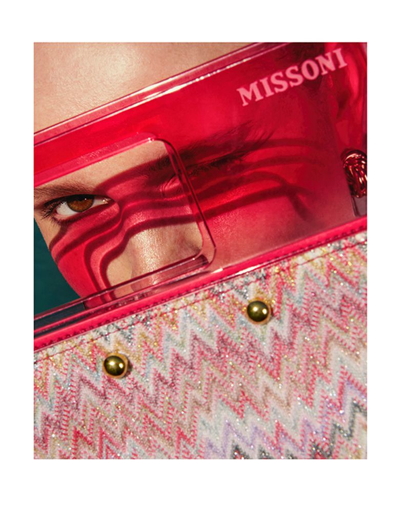 Close-up of a person's face partially obscured by red sunglasses and a patterned handbag, capturing a vibrant fashion detail.