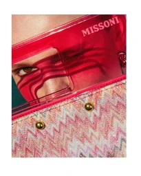 Close-up portrait of a model wearing translucent pink visors and patterned handbag for Missoni SS24 campaign.