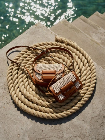 Two woven leather handbags resting on a large coiled rope next to stone steps near glistening water.