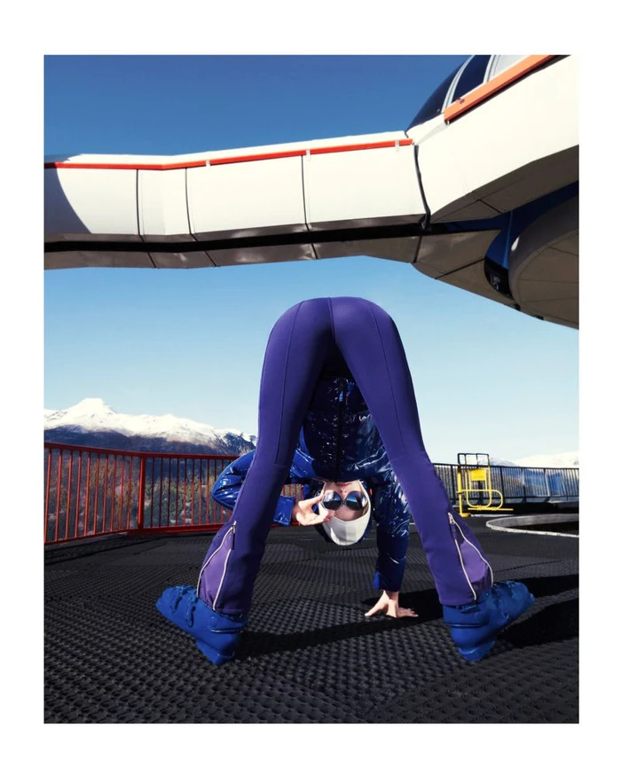 Model in blue ski wear bending over backwards outdoors with snow-capped mountains in the background for the Jet Set campaign.