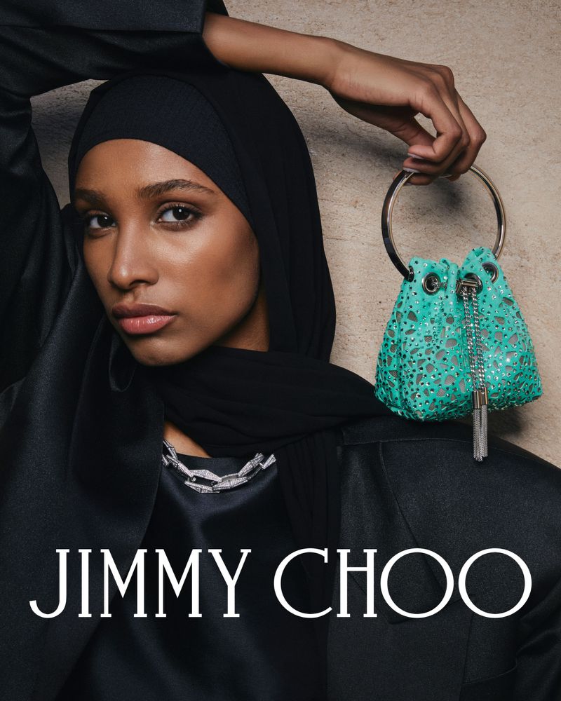 Fashion shot of a stylish woman wearing a black hijab and an elegant black jacket, holding a light blue designer handbag.
