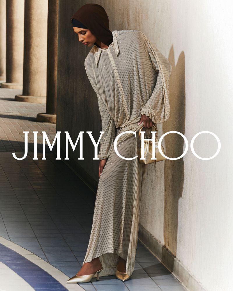 Fashion editorial shot of a woman in a long, sparkly gown with metallic heels and handbag, posing in front of stone columns.