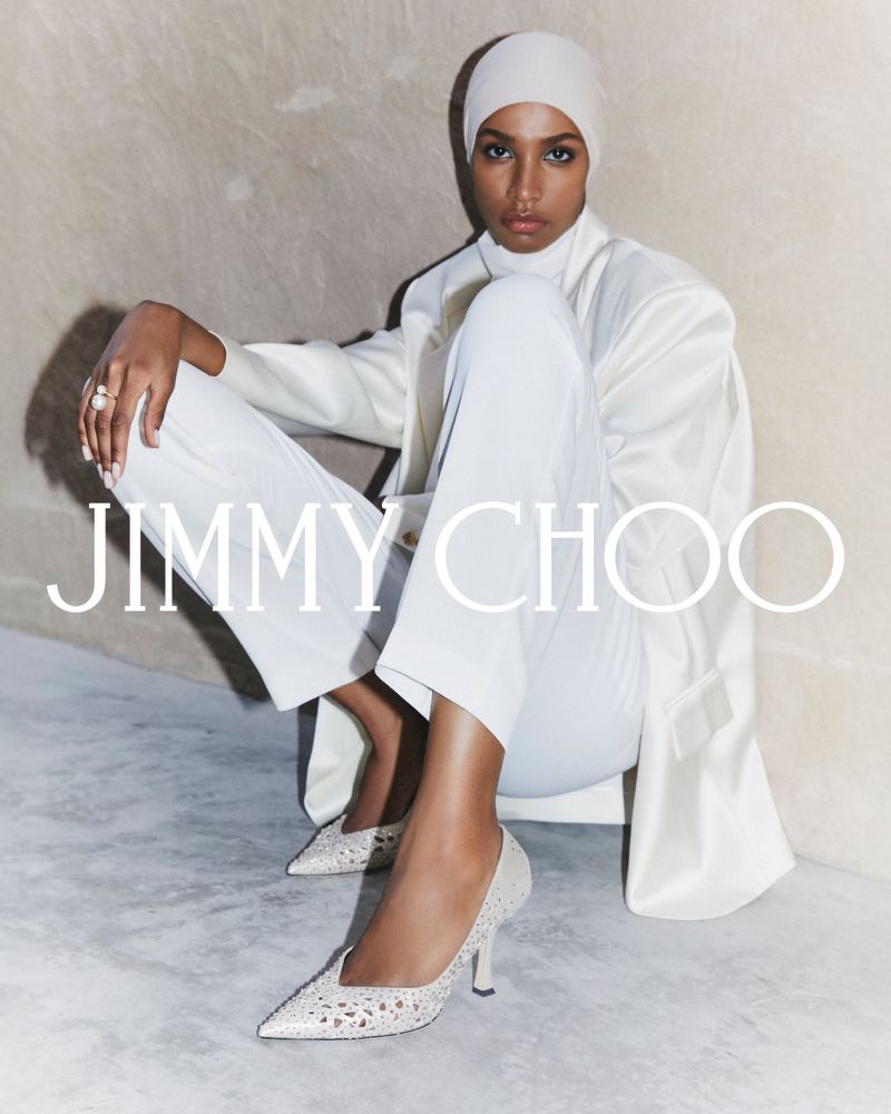 Fashion shot of a woman in an all-white outfit and head covering sitting and posing with Jimmy Choo branded text overlayed on the image.