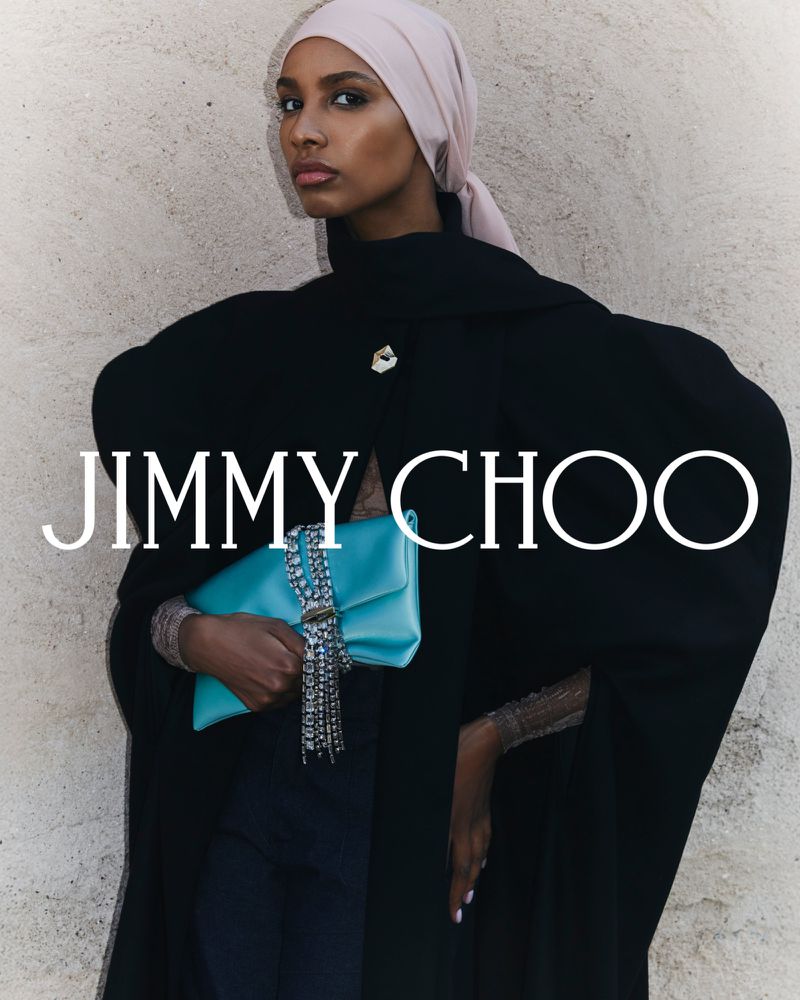 Fashionable woman poses in a black abaya and light pink headscarf, holding a turquoise clutch bag. Jimmy Choo logo on the image.