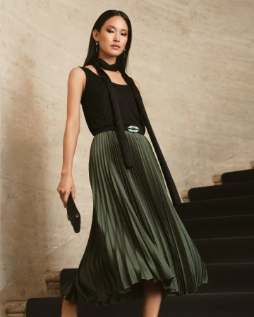 Model wearing a black top and pleated olive green midi skirt descending stone stairs for Ralph Lauren Holiday 24