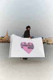 Model carrying a large white branded shopping bag across an open public square in an editorial fashion campaign image