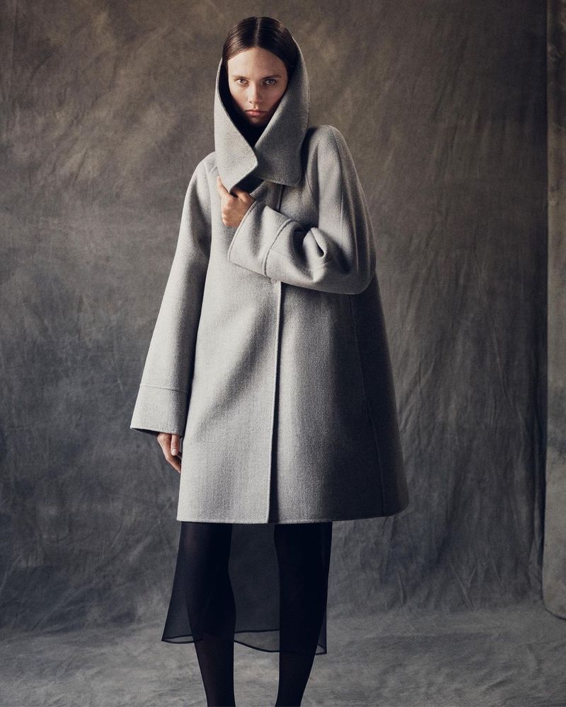 Model wearing a grey hooded coat and black skirt against a textured studio backdrop by photographer Casper Sejersen.
