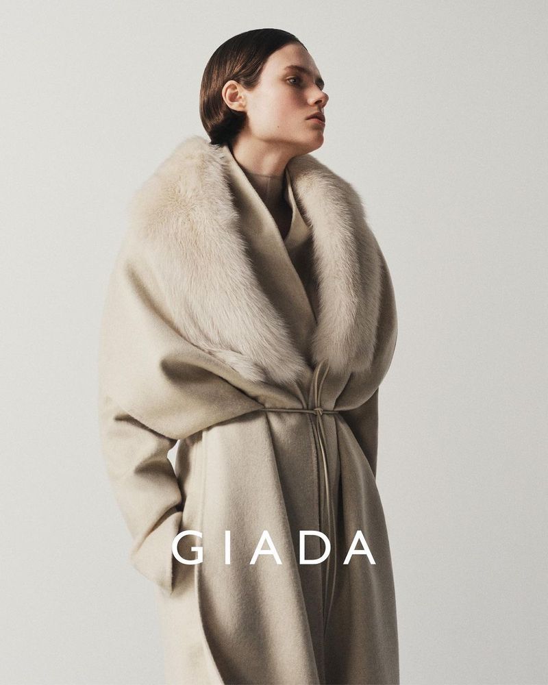 Model wearing a beige wool coat with a fur collar against a light background for Giada