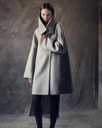 Model wearing a grey hooded coat and black skirt against a textured studio backdrop by photographer Casper Sejersen.