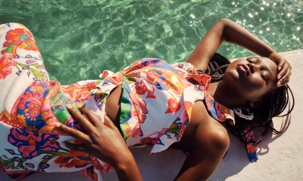 Model Adut Akech in colourful printed Resort RTW apparel lying beside a pool for Zimmermann, photographed by Charles Dennington