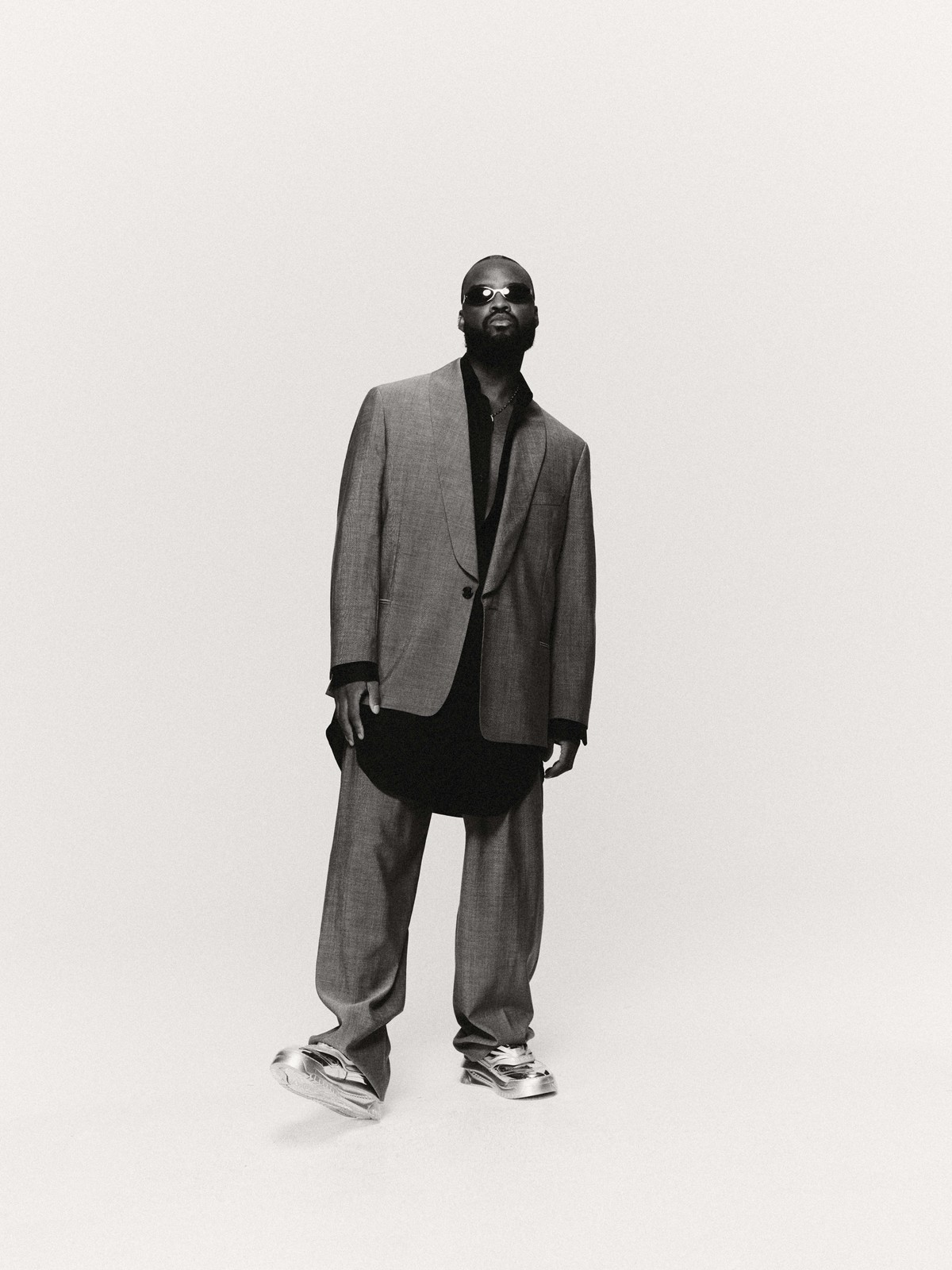 Black and white studio shot of an adult male wearing a suit and futuristic shoes standing in front of a neutral background.
