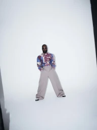 Genesis Owusu in patterned long-sleeve shirt and wide trousers against white backdrop for Esquire Magazine portrait