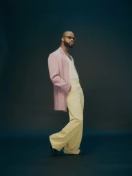 Genesis Owusu in a lilac blazer and light trousers against a dark backdrop for Esquire Magazine
