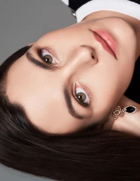 Close-up beauty portrait of a model with dark hair wearing designer earrings against a grey studio backdrop.