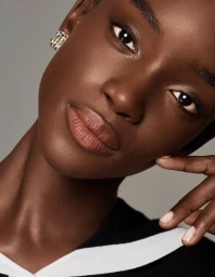 Close-up portrait of model Maty Fall wearing Chanel earrings and black clothing against a neutral grey background
