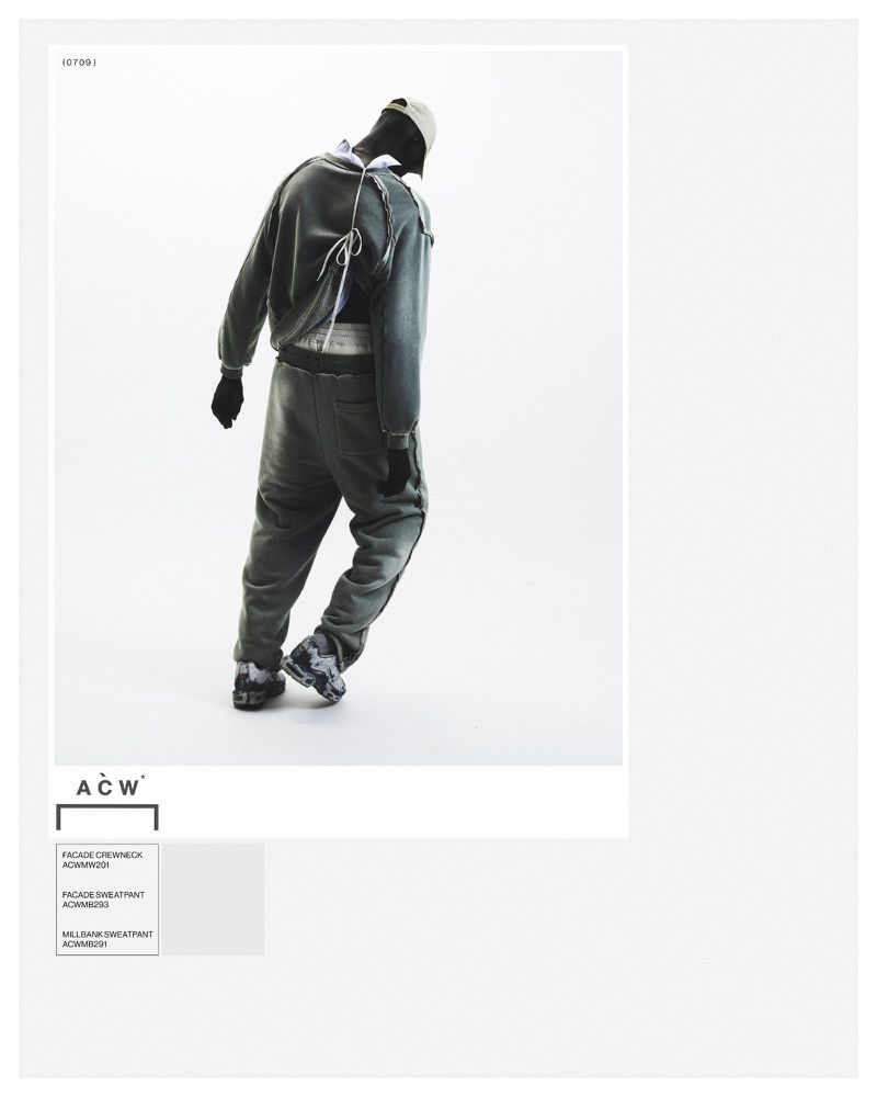 Fashion shot of a person in a gray sweatsuit and cap standing against a bright white background in a high-fashion, studio setting.