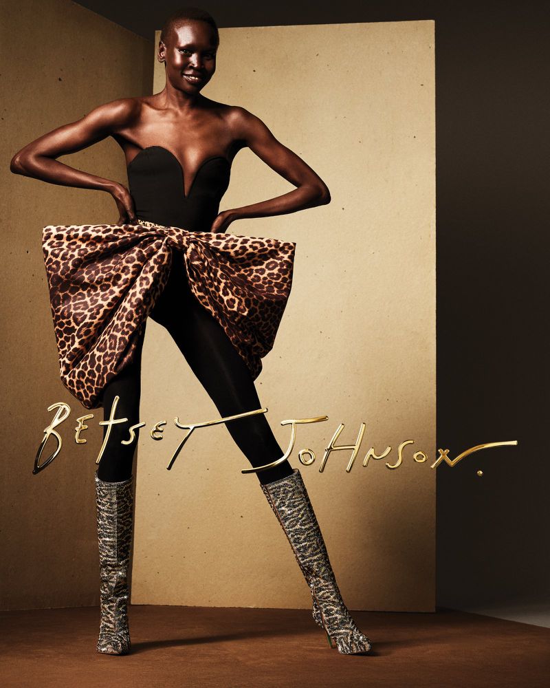 Model Alek Wek wearing a black strapless bodice, leopard print bow bustle, and patterned boots for Betsey Johnson Spring 2025.