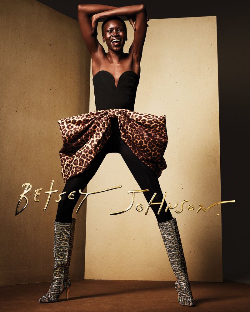 Smiling African American woman in black strapless top, black pants, animal print skirt, and matching boots posing in photo studio.