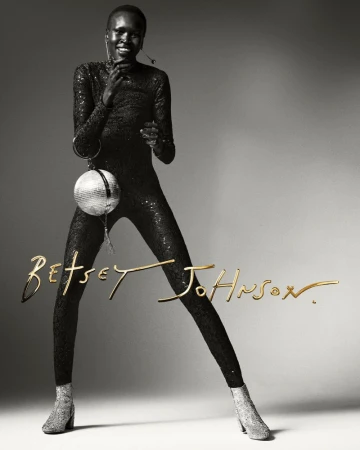 Black and white fashion portrait of a Black female model in a sparkly jumpsuit holding a disco ball, showcasing Betsey Johnson branding.