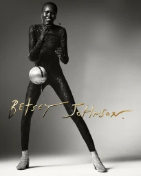 Model Alek Wek wearing a black sequin jumpsuit and holding a spherical disco ball bag for Betsey Johnson Spring 2025 Campaign
