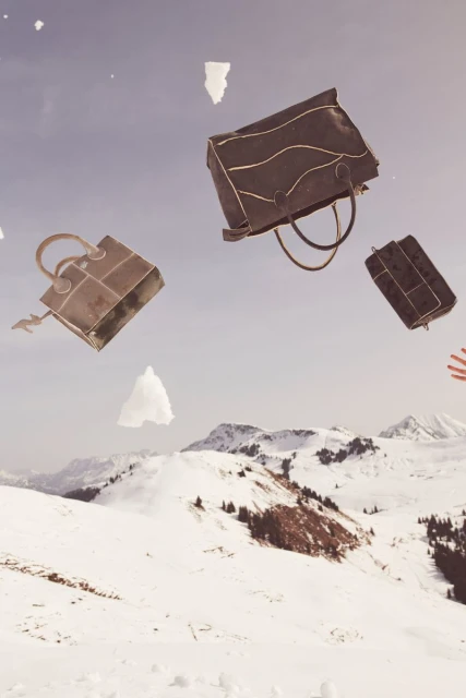Whimsical fashion image: Three brown handbags in mid-air against snow-covered mountains and sky, suggesting a playful, gravity-defying scene.