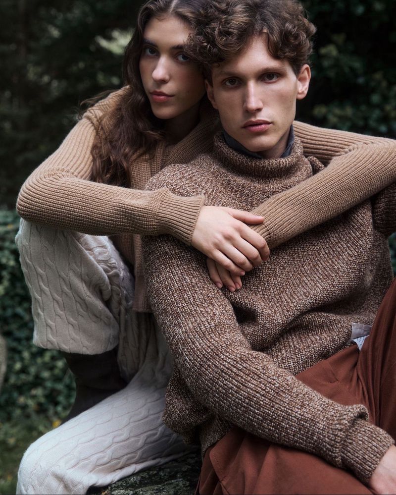 Fashionable couple in matching knitwear poses intimately outdoors in a natural setting, showcasing earthy tones and textures in a portrait-style shot.