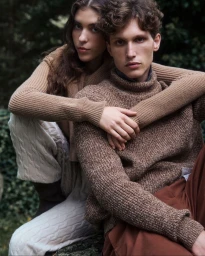 Two models wearing knitwear sweaters outdoors against a blurred natural woodland background.