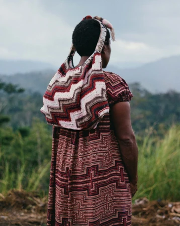 Rear view of a black woman wearing a patterned dress and carrying a knitted shoulder bag outdoors against a mountainous landscape
