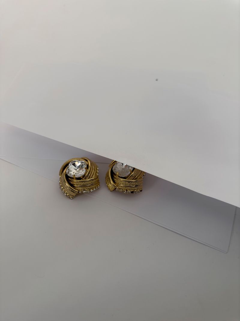 Close-up studio shot of a pair of gold-toned earrings with clear stones on a white surface, showcasing jewelry design.