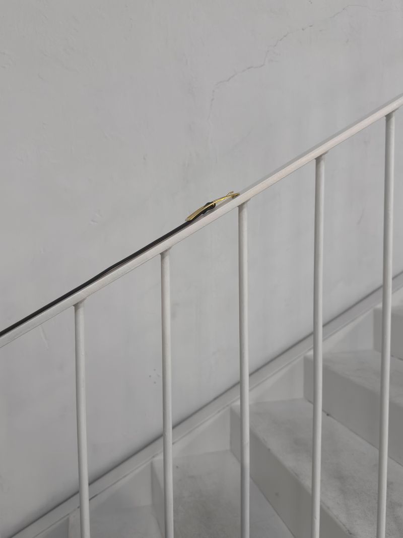 Minimalist shot of white stairs with a white metal handrail and a gold item attached on top in an indoor setting with natural light.