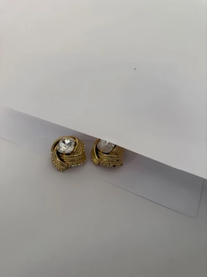 Pair of ornate gold earrings with central square crystals displayed against a plain white studio background.