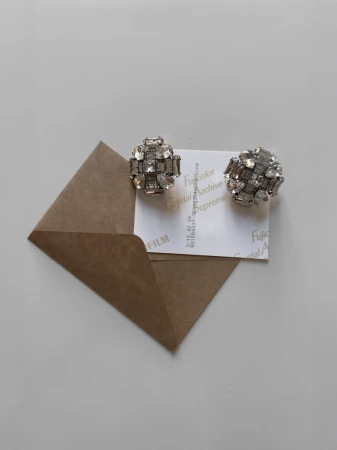 Sparkling crystal earrings resting on a small white card inside an open brown paper envelope.