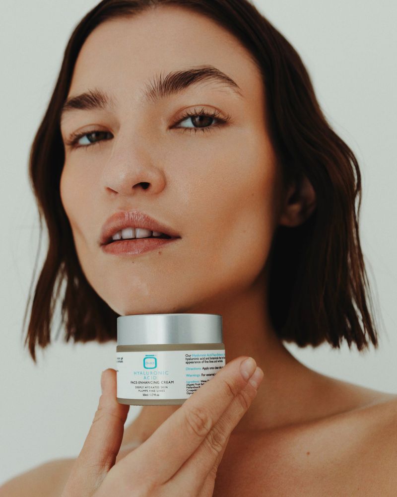 Woman showcases a skincare cream product in a studio setting, highlighting beauty and personal care, set against a clean, white background.