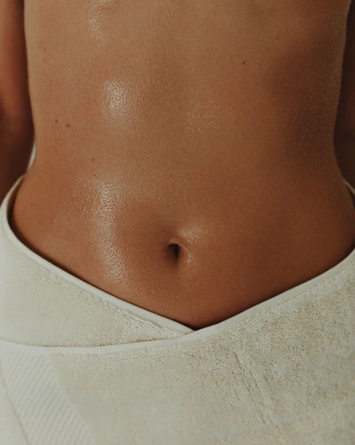 Close-up shot of a woman's tanned abdomen wrapped in a white towel, emphasizing skincare and body wellness.