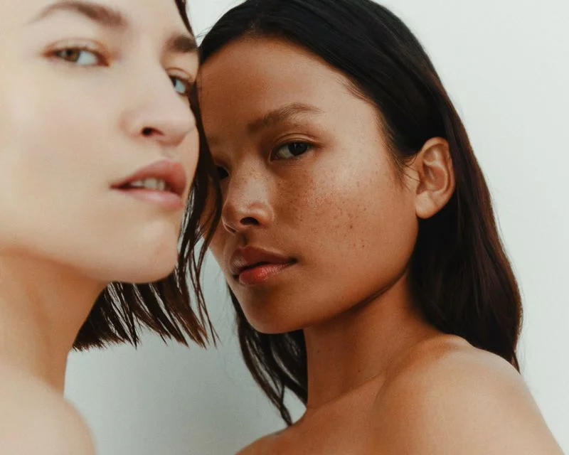 Close-up beauty portrait of two female models posing against a neutral white background