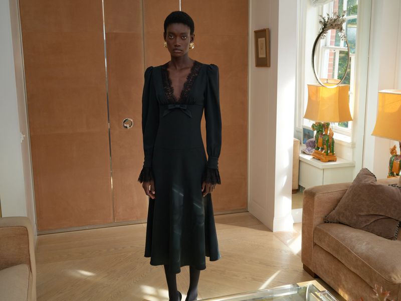 Elegant African-American woman in a black lace dress with long sleeves poses in a home interior with a tan closet and sofa.