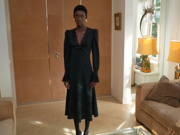 Elegant African-American woman in a black lace dress with long sleeves poses in a home interior with a tan closet and sofa.