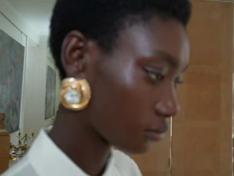 Close-up portrait of a model with short dark hair wearing ornate gold earrings and a white top