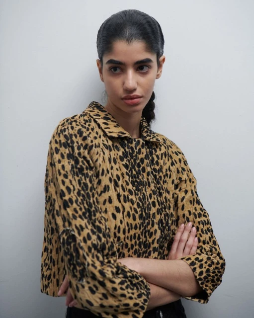 Portrait of a woman wearing a leopard-print jacket against a grey wall, showcasing fashion and a neutral background.
