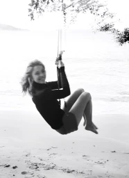 Sydney Sweeney swinging on a rope swing over a sandy beach in a black top