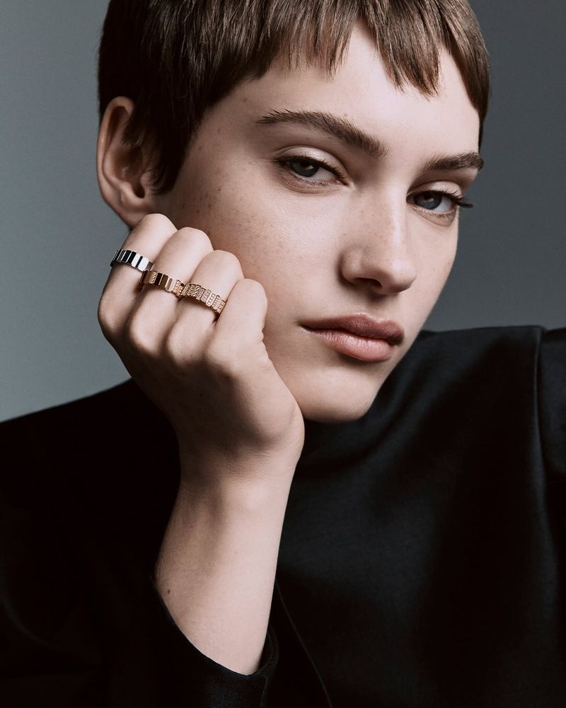 Close-up studio portrait of a young woman wearing two block-design rings on one hand, dressed in a black turtleneck sweater.