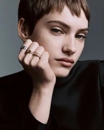 Model wearing stacked rings on her hand resting under her chin against a grey background for Dior Gem