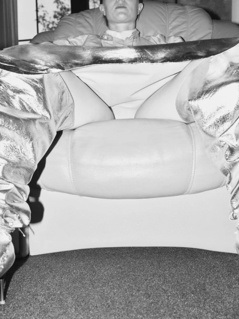 Black and white studio shot of a person lounging in a chair wearing shiny, metallic boots, capturing a unique perspective and style.