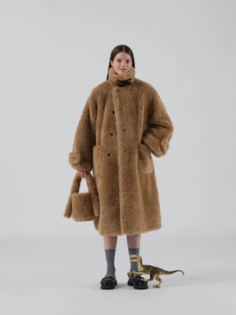A young woman poses in a full-length shot, wearing an oversized brown faux-fur coat with a matching purse, against a neutral background.