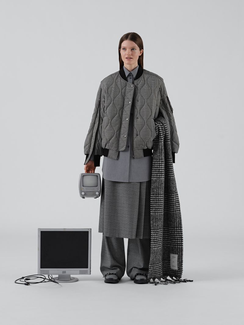 Adult female fashion model poses with a vintage television and computer monitor in a studio wearing grey tone patterned clothing.