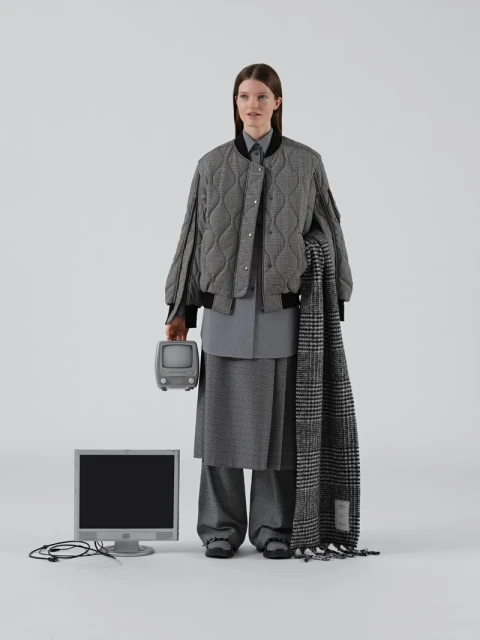 Adult female fashion model poses with a vintage television and computer monitor in a studio wearing grey tone patterned clothing.