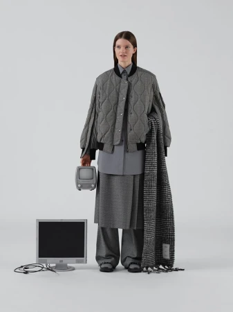 Adult female fashion model poses with a vintage television and computer monitor in a studio wearing grey tone patterned clothing.